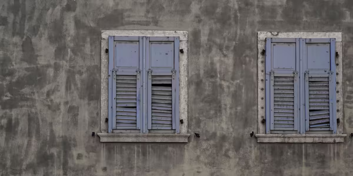 Deux fenêtres aux volets bleus fermés sur une façade grise
