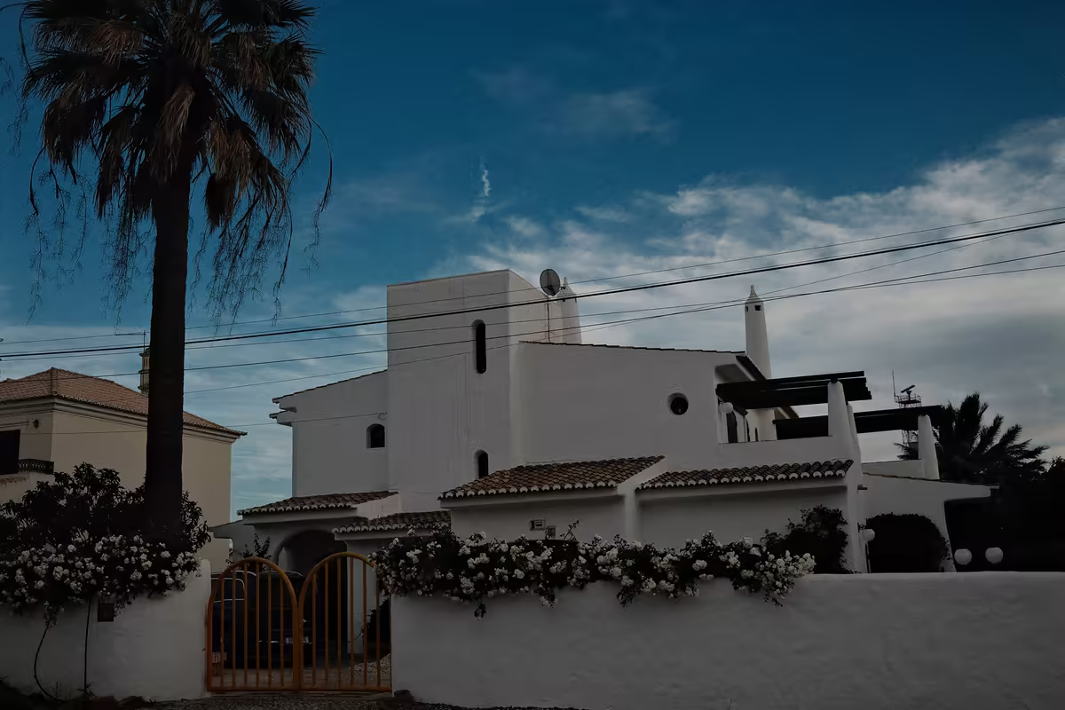 Maison blanche de style méditerranéen derrière son mur et son portail fermé, sous un ciel du soir