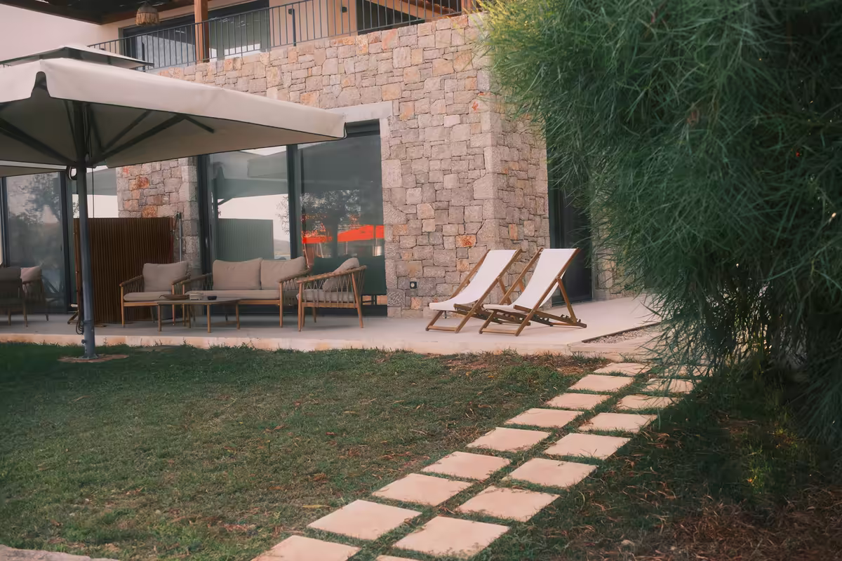 Terrasse en pierre avec parasol et transats vides, au bord d'une pelouse entretenue