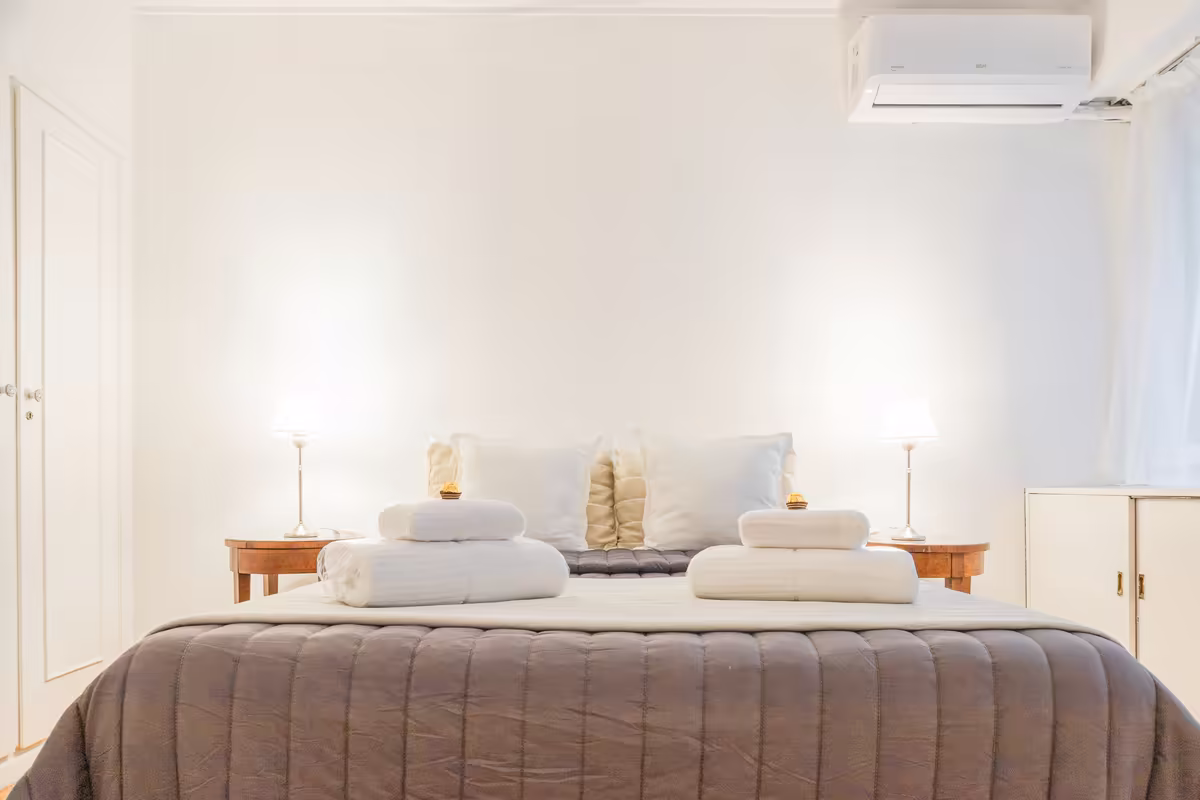 Bright bedroom with a made bed and folded towels laid on it