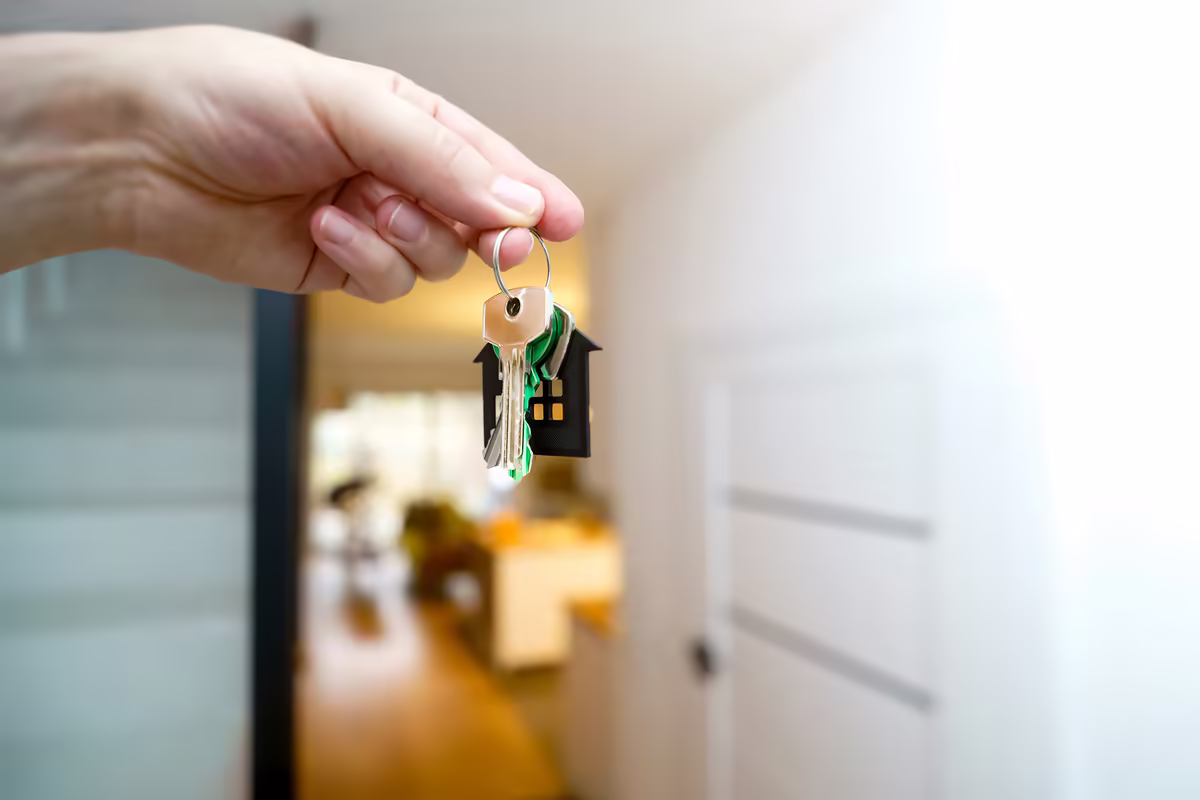 Hand holding a set of keys in front of a half-open front door